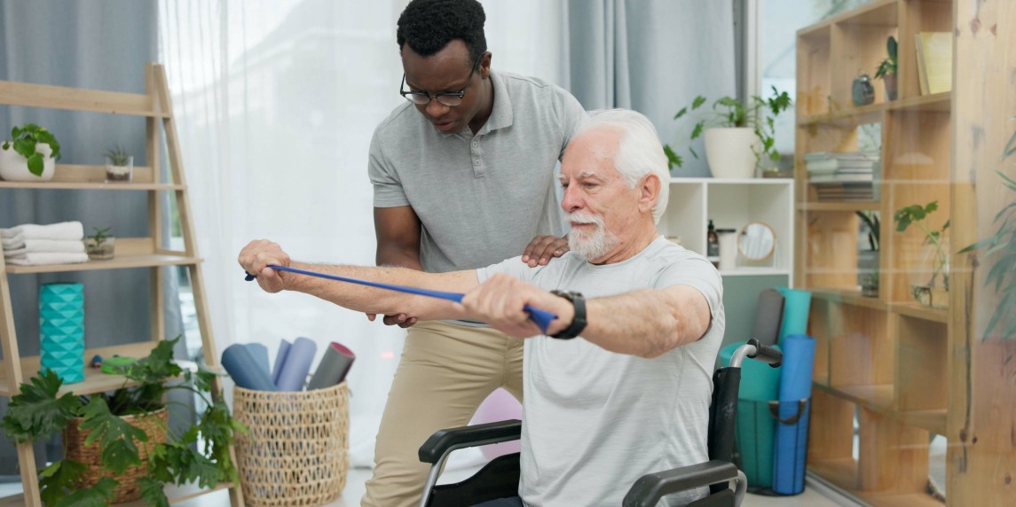 Senior man with disability, physiotherapist and stretching band for muscle rehabilitation, chiropractor service or help. Physical therapy, medical support or patient in wheelchair at recovery clinic