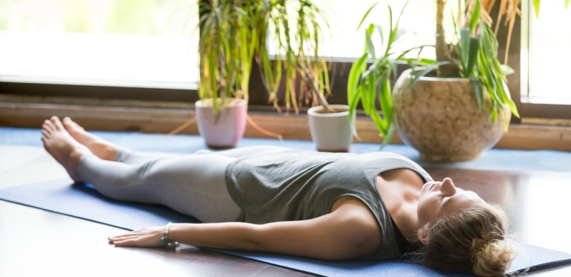 Quad Clenche: Attractive young woman working out at home, doing yoga exercise on blue mat, lying in Shavasana (Corpse or Dead Body Posture), resting after practice, meditating, breathing. Full length