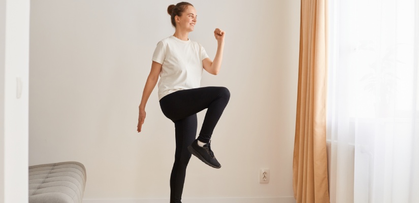 Knee marching: Full length portrait of slim athletic woman wearing white t shirt and black leggins doing sport exercises at home on yoga mat, walking in place, marching, sport, fitness at home.