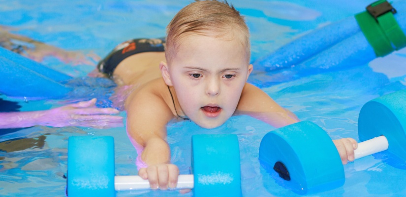 A little boy with Down syndrome swims in the pool. Teaching children to swim. Sports. Active healthy lifestyle in children. Health care.