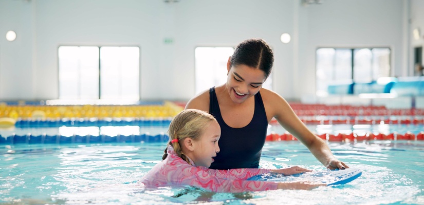 Instructor, teaching and child in pool, swimming or woman with smile, proud or helping girl in water. Bathing suit, happy or learning with teacher in school for training of kid, sports or competition